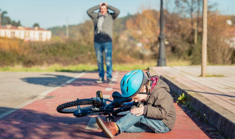 Boy in helmet crying after falling off his bike with father distressed