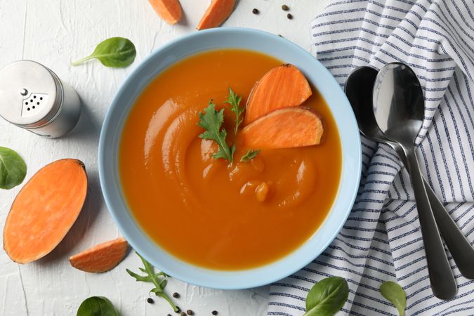 Sweet potato soup on table with kitchen towel, salt pepper and spoons