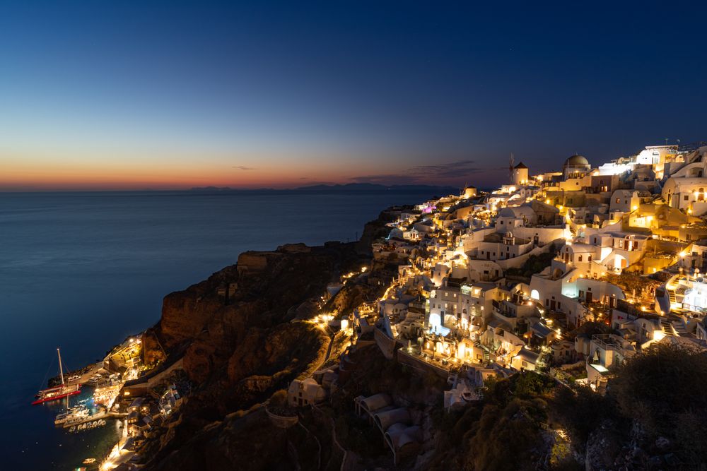 Buildings overlooking the sea lit up at as night falls