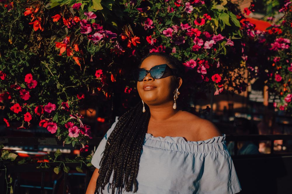 Joyful trendy Black woman in sunglasses standing beside blossomed tree