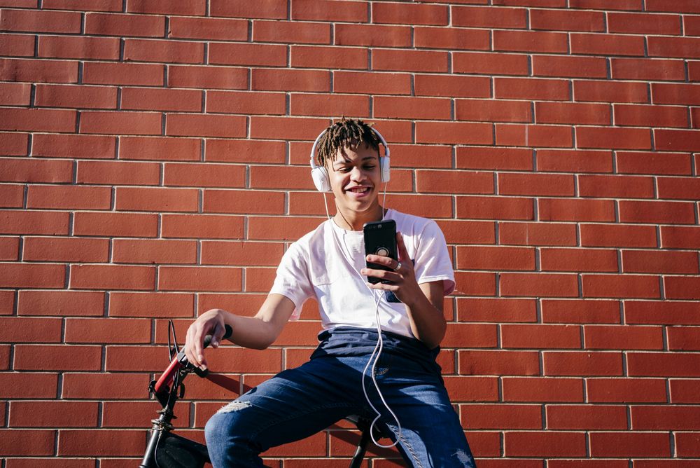 Young happy Black male listening music with smartphone on bike