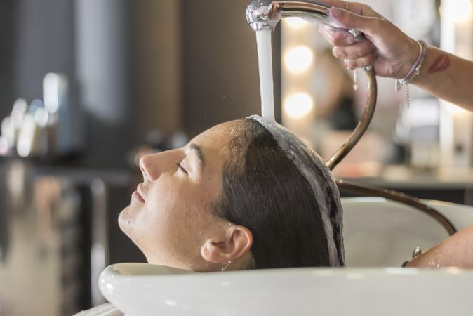 Relaxed female lying back having her hair washed by stylist
