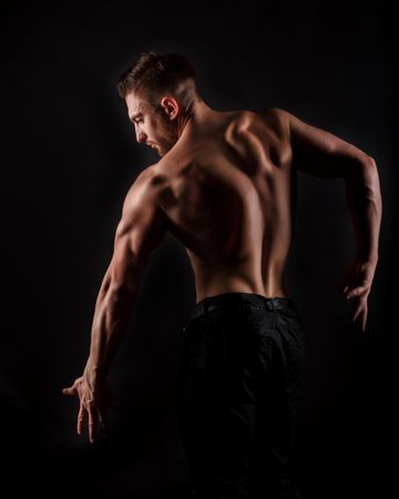 Bodybuilder practicing back poses ahead of competition in dark studio