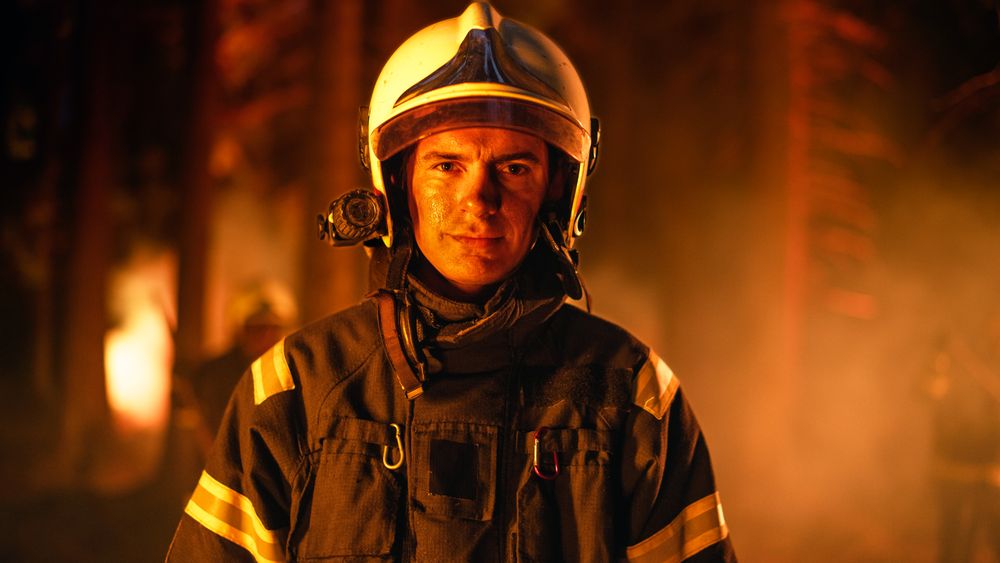 Portrait of a Confident and Young Adult Firefighter in Safety Uniform and a Helmet with a Flashlight.
