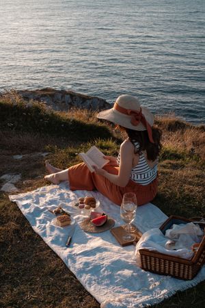 Woman reading on mat for picnic on seashore