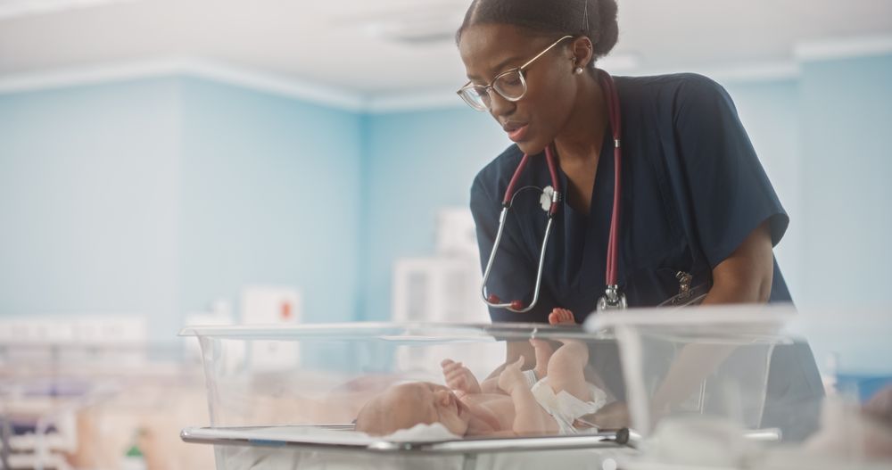 Black Pediatrician Putting the Infant Back in the Bassinet During a Checkup in Nursery