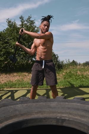 Muscular Black guy hammering tire in outdoor gym