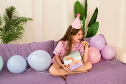 Girl laughing with party hat and holding birthday gifts.