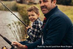 Young child holding fishing rod with father and looking at camera 5rqX70