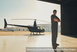Man standing tall with arms crossed in helicopter hangar on sunny day 0PZMg4