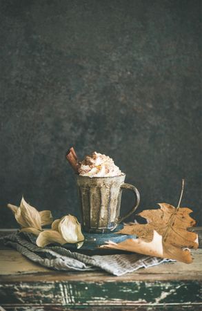 Mug of warm drink topped with whipped cream and cinnamon sticks, on dark background, copy space