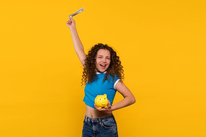 Excited girl celebrating with money and piggy bank in hand