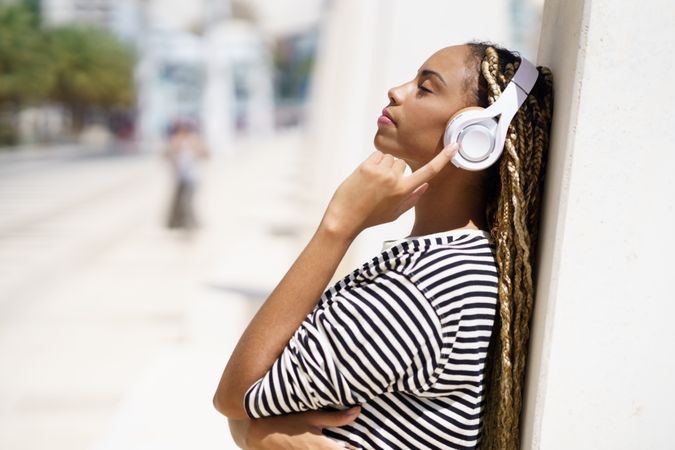 Female leaning on wall and listening to music on headphones on sunny day