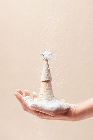 Woman’s hand holding Christmas tree made from waffles cones and powdered sugar snow