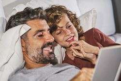 Curious boy and father reading book on bed