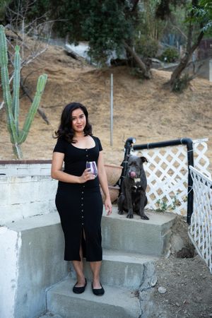Beautiful woman in dark dress holding a glass of wine standing in front of hillside