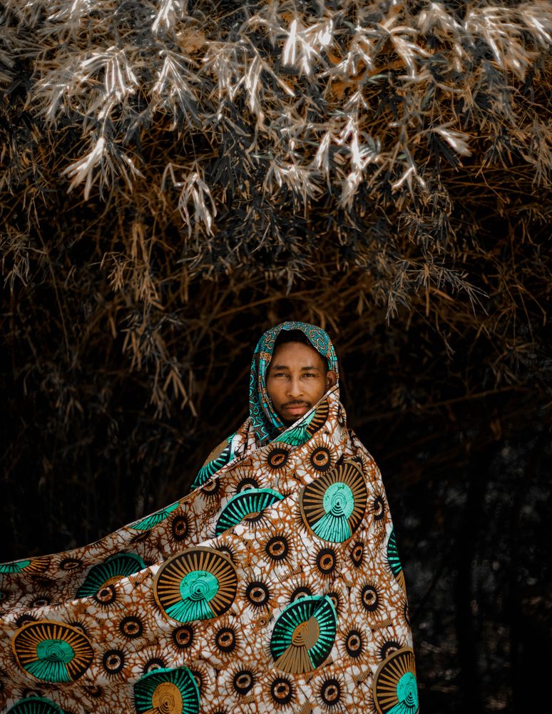 Man covering his head with scarf standing beside tree