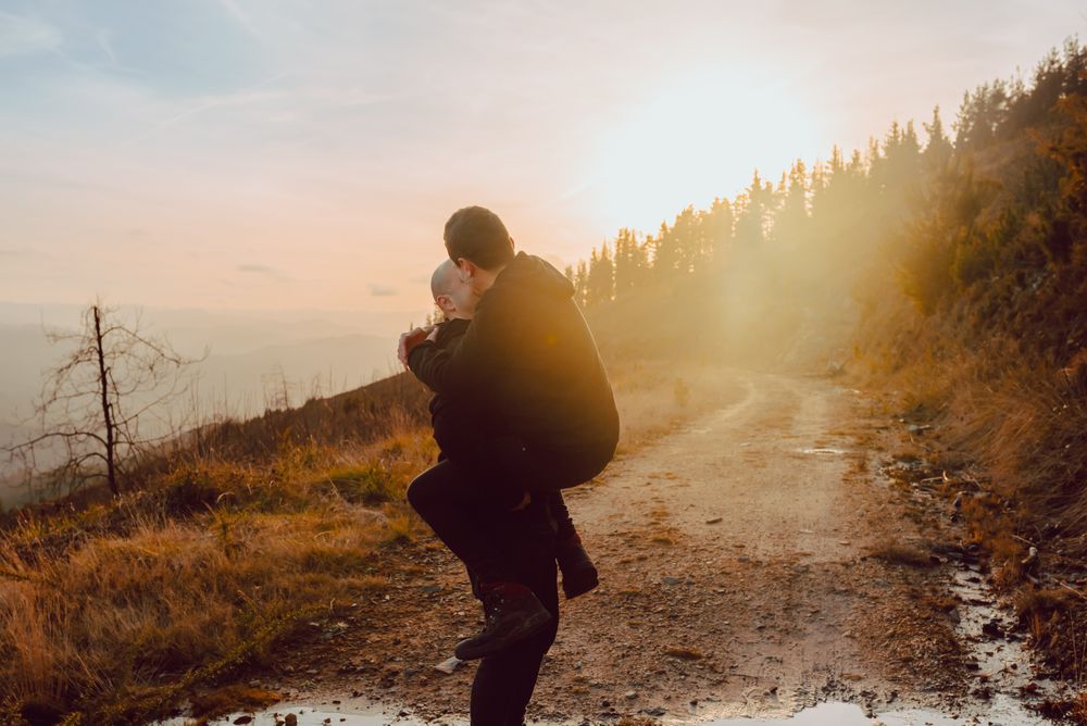 Smiling man holding cheerful guy on road on hill