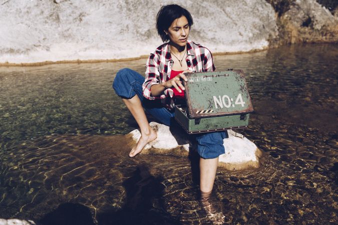 Woman with picnic case on rock in water