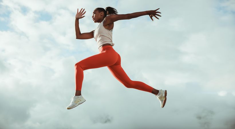 Athletic woman running and jumping outdoors against sky