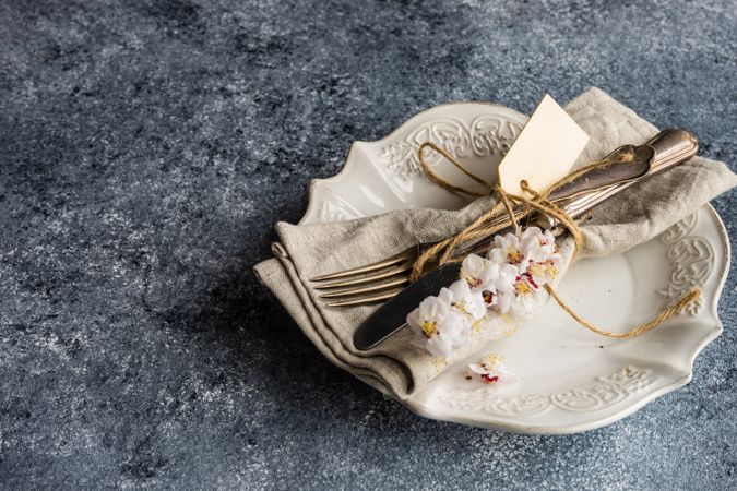 Spring floral concept with top view of apricot blossom branches surrounding cream plates on grey table