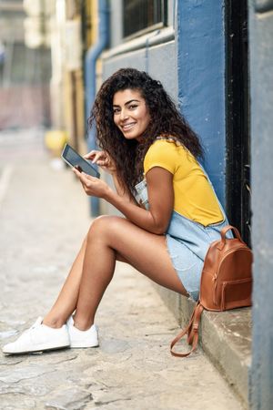 Arab woman looking at her digital tablet sitting outside a door, vertical