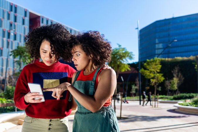 Female couple discussing something on smartphone outside