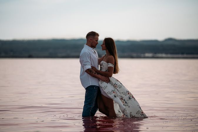 Side view of adorable couple embracing into an amazing beach with pink water