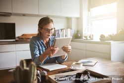 Woman holding and reading tablet at kitchen table 0ylG7b
