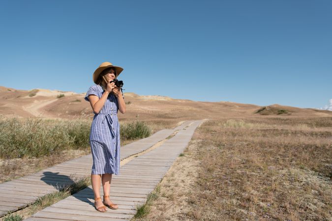 adult woman in straw hat and dress with camera standing on country path