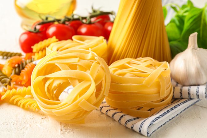 Composition with pasta, tomatoes, garlic, olive oil and kitchen towel on light background, space for text and closeup