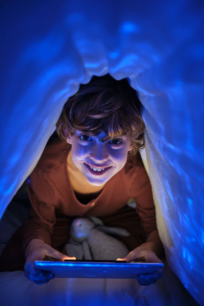 Content boy playing on tablet under blanket