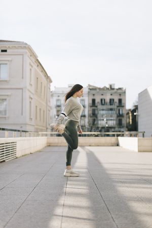 Woman stretching her quads out on a rooftop in a city