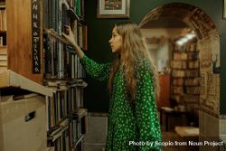 Girl in green polka dot dress taking a book from bookshelves 5Qdng0