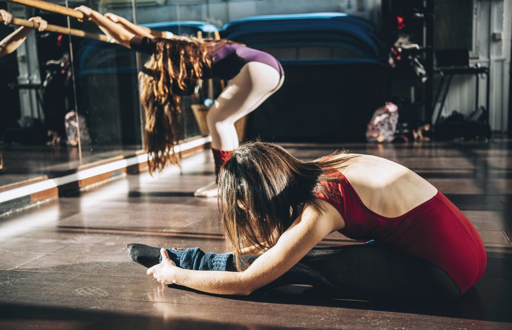 Side view of ballerinas warming up and stretching in bright ballet studio.
