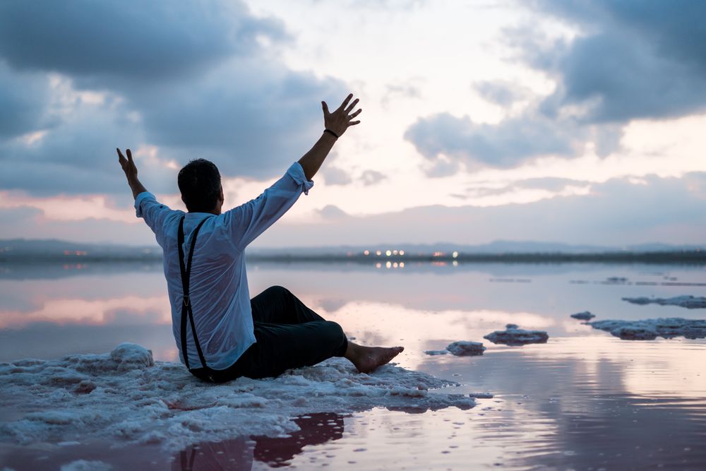 Relaxed man standing with outstretched hands with empty fish tank at shore