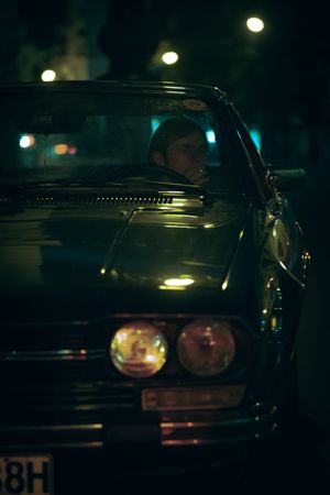 Young man sitting on driver seat of an old car at night