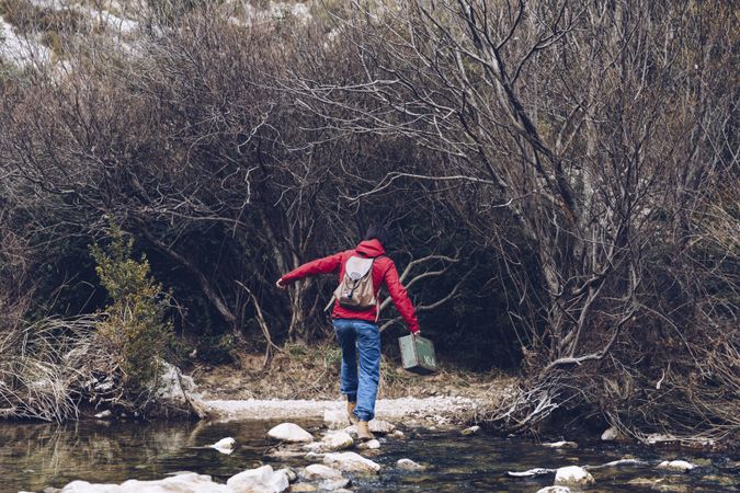 Woman with case jumping on rocks above stream
