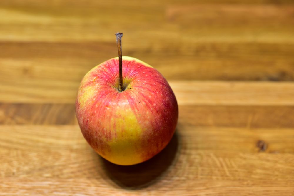 A crisp, red apple sits enticingly on a rustic wooden table