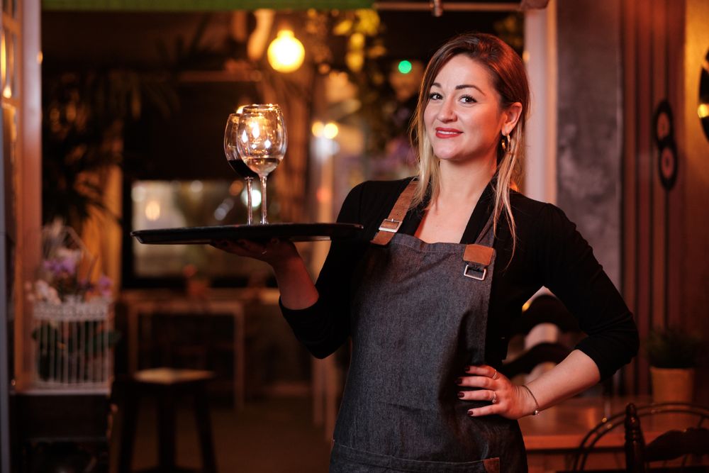Cheerful waitress holding tray with wineglasses