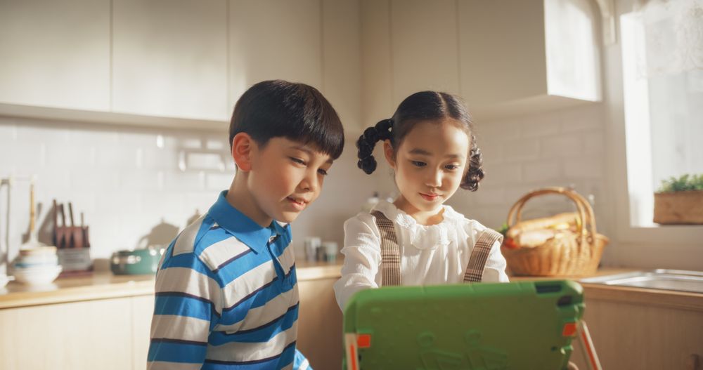 Portrait of Two Korean Kids Using a Digital Tablet During Weekend in The Kitchen.