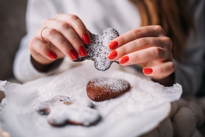Woman with manicured hands holding a festive gingerbread cookie over a trey