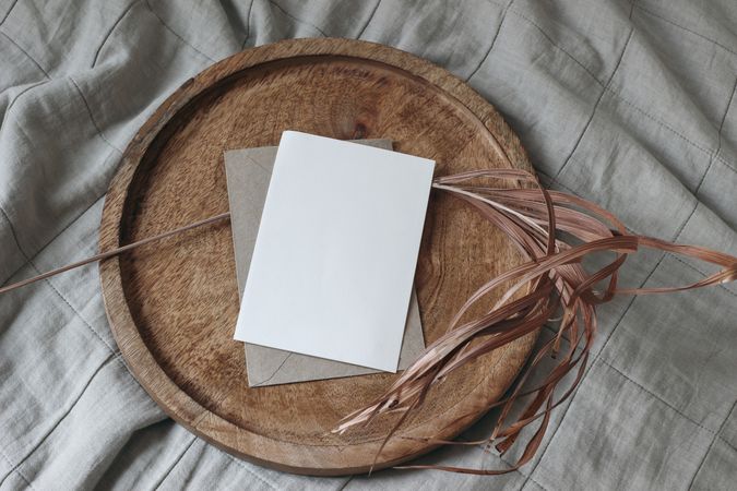 Blank greeting card mockup on wooden tray with dry palm leaf