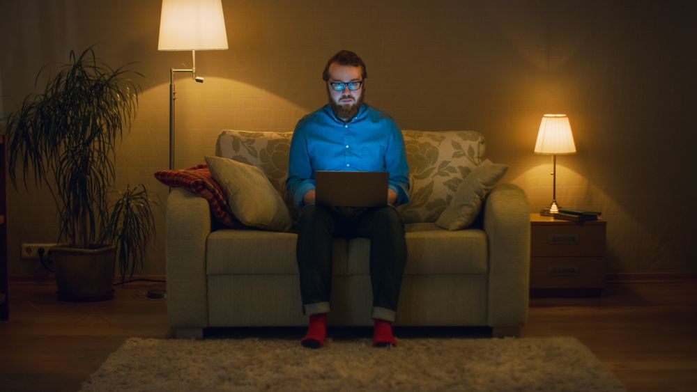 Portrait Shot of a Man Sitting on a Couch in His Living Room, Laptop on His Knees.