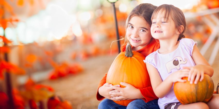 Two Girls Holding Their Pumpkins At A Pumpkin Patch on a Fall Day.