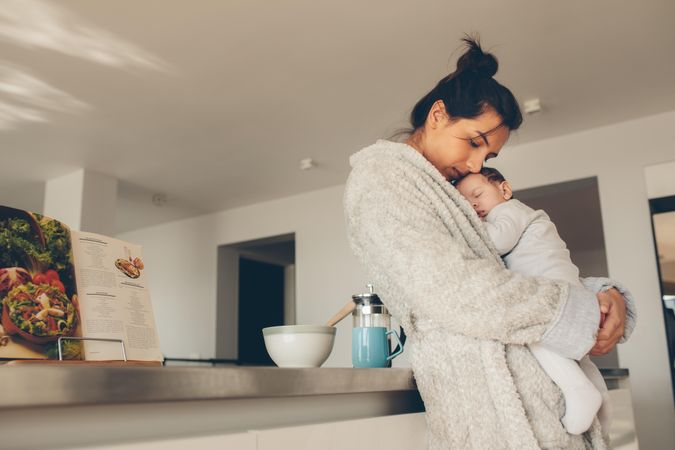Loving mother carrying her newborn baby boy and standing in kitchen