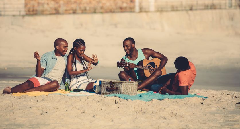 Young man playing guitar for friends at picnic on the coast