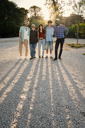 Full length portrait of a diverse group of friends standing together outdoors at sunset.