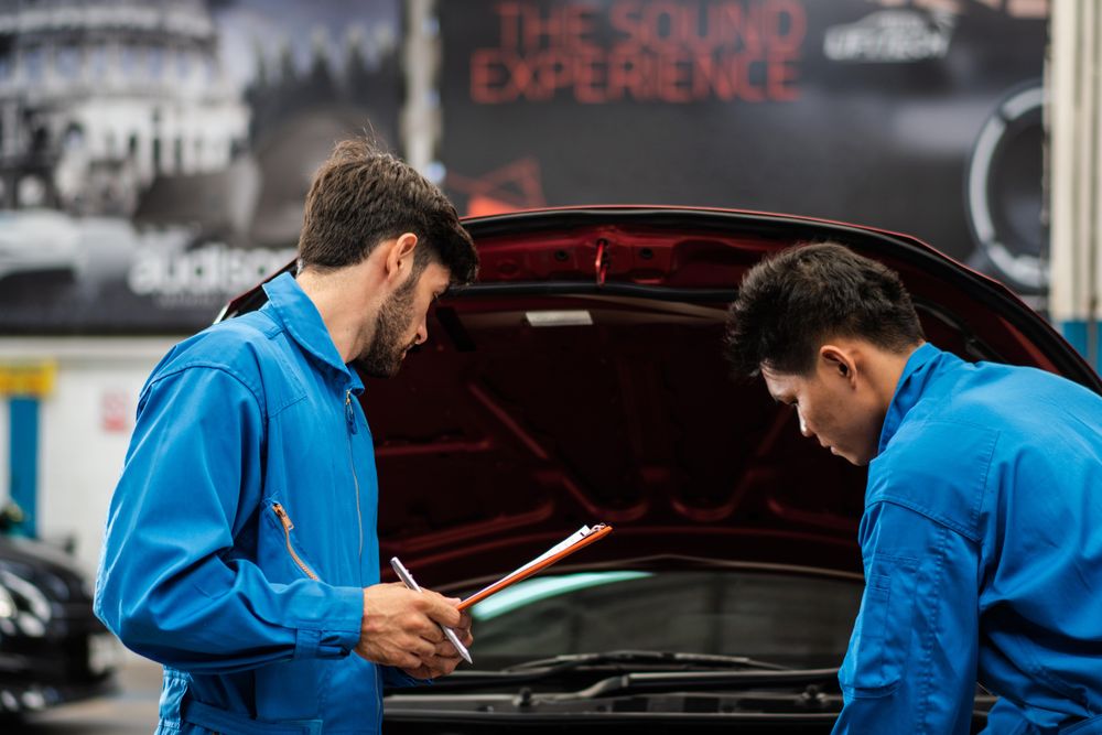 Two male auto workers standing working at open engine