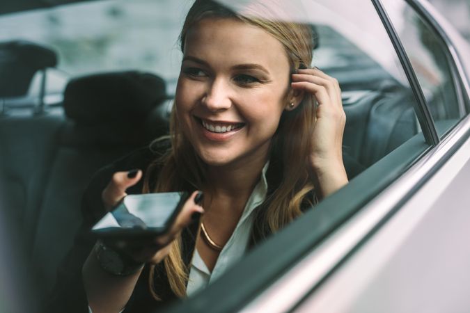 Happy young businesswoman talking on the mobile phone while sitting on back seat of a car